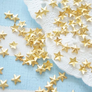 May include: A scattering of gold glitter star-shaped embellishments on a blue and white striped surface and a white doily.