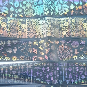 Może przedstawiać: Zestaw 10 iryzujących holograficznych naklejek do zdobienia paznokci z różnymi wzorami, w tym piórami, łapaczami snów, kołami zębatymi, gwiazdami, rakietami, kształtami geometrycznymi i wzorami plemiennymi.