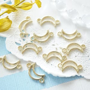 May include: A collection of gold-toned metal crescent moon charms with open centres. The charms have two small loops on each side for attaching to jewellery or other crafts.