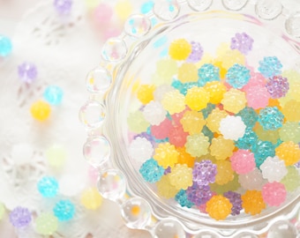 May include: A clear glass bowl filled with colorful candy sprinkles. The sprinkles are in shades of pink, blue, yellow, and purple.