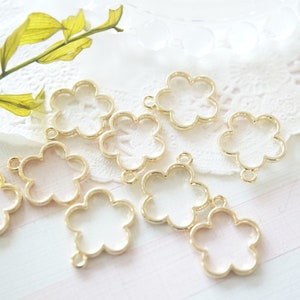 May include: A set of eight gold-toned metal flower-shaped pendant frames. The frames are open and have a smooth, polished finish.