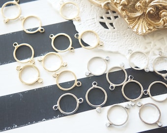 May include: A collection of gold and silver metal jump rings with two loops on each ring. The rings are arranged on a black and white striped surface.