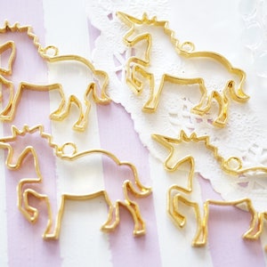 May include: Five gold-colored metal unicorn charm blanks. The charms are in the shape of a unicorn with a horn, mane, and tail. The charms are on a white background with a lace pattern.