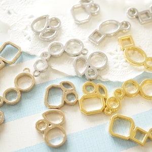 May include: Various geometric metal jewellery findings in gold and silver tones. The findings feature circles, squares, and teardrop shapes, connected in different arrangements. The background has a light blue and white striped pattern.