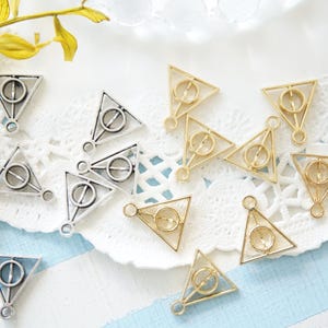 May include: A collection of silver and gold triangle charms with a circle in the centre. The charms are arranged on a white lace doily.