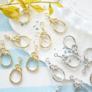 May include: A collection of gold and silver metal jewelry findings with a knot design. The findings are in the shape of a circle with a loop at the top. They are perfect for making earrings, necklaces, and bracelets.