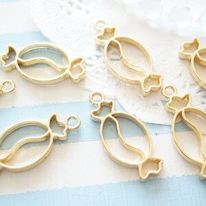 May include: Seven gold-coloured metal candy charm pendants. Each pendant is shaped like a candy with a swirl design. The pendants have a hole at the top for attaching to a chain or other jewellery.