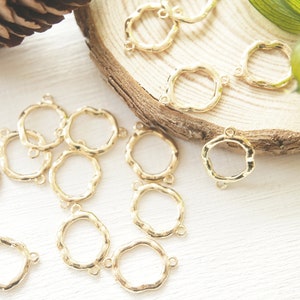 Könnte beinhalten: Eine Sammlung von 14 goldfarbenen Metall-Verbindungsringen mit einer strukturierten, unregelmäßigen, kreisförmigen Form. Jeder Ring hat zwei Sprungringe.