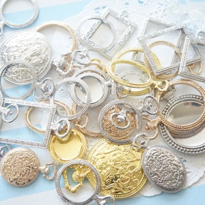 Puede incluir: Una colección de dijes y colgantes de metal plateado y dorado, que incluyen círculos, cuadrados y diseños ornamentados. Los dijes están dispuestos sobre un fondo de encaje blanco.