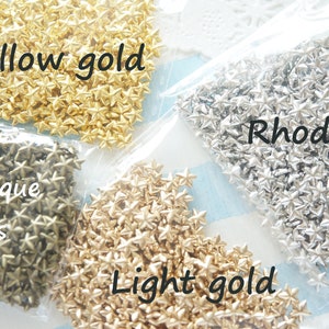 Puede incluir: Cuatro bolsas de adornos metálicos en forma de estrella en diferentes acabados: latón antiguo, oro claro, oro amarillo y rodio.