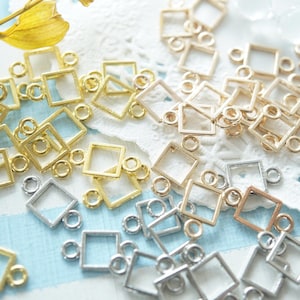 May include: A collection of small, square-shaped metal jewelry connectors in gold, silver, and rose gold tones. Each square frame features two small circular loops on opposite sides, designed for linking components in jewelry making projects.