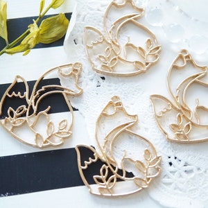 May include: Four gold-colored metal fox charms with intricate cut-out designs. Each charm features a fox with a curled tail and leaves surrounding it.