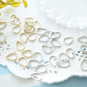 May include: A close-up of a white lace doily with a variety of gold and silver teardrop-shaped metal charms. The charms are scattered across the doily, creating a decorative and elegant display.