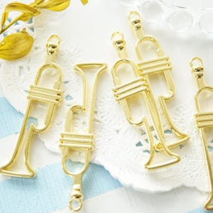 Puede incluir: Seis abalorios de trompeta de metal de color dorado con un diseño delicado. Los abalorios son perfectos para añadir un toque musical a las joyas o las manualidades.