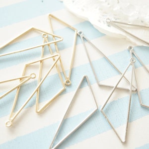 May include: Various geometric earring components in gold and silver. The components are diamond-shaped with a small loop for attachment. The background features a light blue and white striped pattern, typical of a seaside theme.
