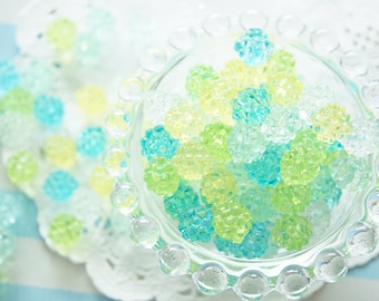 May include: A clear glass bowl filled with small, round, green and blue candy. The bowl has a decorative, scalloped edge.