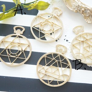 May include: Four gold-coloured metal charms with geometric designs. The charms are in the shape of a circle with a star, a circle with a star and a circle inside, a circle with a star and a circle inside, and a circle with a geometric pattern.