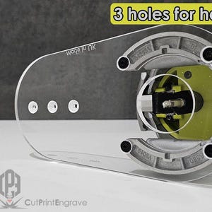 May include: A clear plastic extended router base plate for Ryobi ONE+ P601 and PCL424B routers. The plate has three holes for a handle and the text "V8019 ni ebom 842851" is printed on the side. The plate is designed to fit over the router and provide a larger base for more stability.
