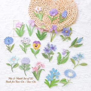 May include: A collection of twenty embroidered flower patches in shades of blue, purple, pink, and yellow with green stems and leaves. One patch is labeled with a 3 inch measurement indicator. The text reads: Mix & Match Set of 20 Back for Iron-On / Sew-On.