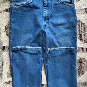 Pu&ograve; includere: Jeans blu in denim con un classico design a cinque tasche. I jeans hanno una chiusura con bottone e cerniera, passanti per cintura e rivetti color rame. Il tessuto ha un lavaggio medio e un aspetto leggermente usurato.
