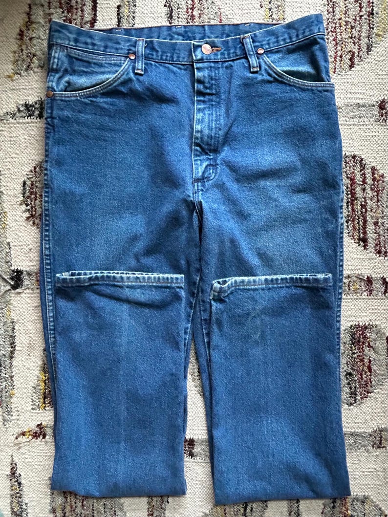 Pu&ograve; includere: Jeans blu in denim con un classico design a cinque tasche. I jeans hanno una chiusura con bottone e cerniera, passanti per cintura e rivetti color rame. Il tessuto ha un lavaggio medio e un aspetto leggermente usurato.