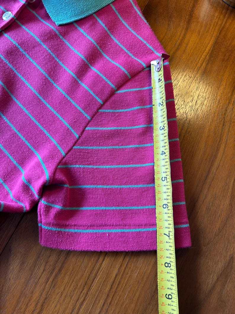 Może przedstawiać: Koszulka polo w paski r&oacute;żowe i zielone z taśmą mierniczą pokazującą długość rękawa 17,8 cm.
