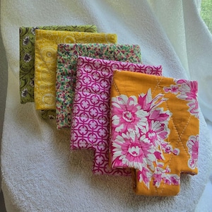 May include: A set of five square fabric coasters featuring various patterns including a green floral print, a yellow geometric design, a multi-colored floral pattern, a pink circular lattice print, and an orange fabric with large pink flowers.