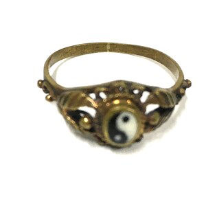 Peut inclure: Une bague dor&eacute;e avec un symbole yin yang en noir et blanc sur fond blanc. La bague a un design d&eacute;licat et orn&eacute;.