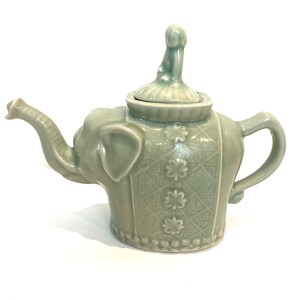 May include: A light green ceramic teapot shaped like an elephant with a patterned design and a small elephant finial on the lid.