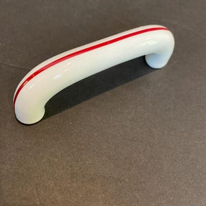 May include: White ceramic cabinet door handle with a red stripe down the center.