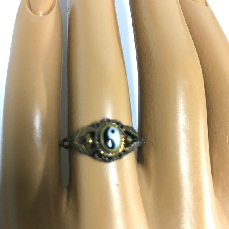 Peut inclure: Une bague en or avec un symbole yin yang noir et blanc sur fond blanc. La bague est port&eacute;e sur un doigt.