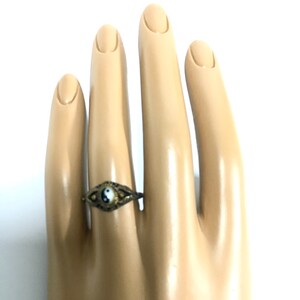 Peut inclure: Une bague en or avec un symbole yin yang noir et blanc sur une main de mannequin.