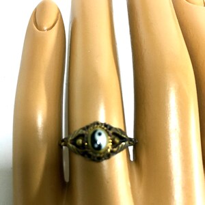 Peut inclure: Une bague en or avec un symbole yin yang noir et blanc sur fond blanc. La bague est sur un doigt de mannequin.