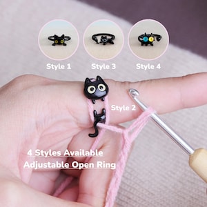 Könnte beinhalten: Vier schwarze Ringe in Katzenform mit verstellbarem offenem Design. Die Ringe werden auf einem Finger mit rosa Garn und einer Häkelnadel gezeigt. Der Text auf dem Bild lautet: "4 Styles Available Adjustable Open Ring."