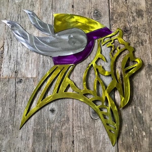 May include: A metal wall art sculpture of a Viking helmet with a purple and gold design. The helmet is made of metal and has a detailed design.
