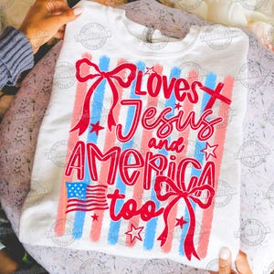 May include: White sweatshirt with a patriotic design. The design includes red and blue stripes, a small American flag, stars, and the text "Loves Jesus and America too" in red script.