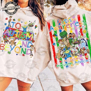 May include: A beige hoodie with the text "TO AUTISM AND BEYOND" and "Autism Awareness and beyond". The design features cartoon characters and puzzle pieces in various colors. The hoodie promotes acceptance, inclusion, and advocacy.