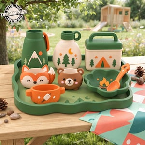 Puede incluir: Una bandeja verde con artículos de camping que incluyen un termo verde, una botella blanca, una fiambrera verde, un cuenco con forma de zorro, una taza con forma de oso, un cuenco naranja con un malvavisco y un cuenco con forma de flor con cuchara.