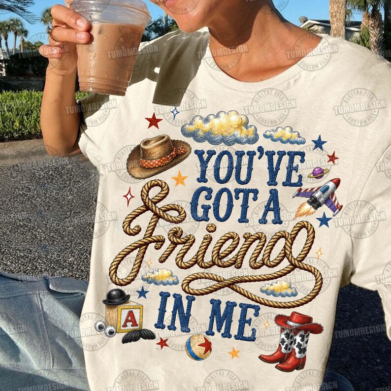 May include: A cream-colored t-shirt featuring the blue text "YOU'VE GOT A FRIEND IN ME" surrounded by a brown rope graphic, a cowboy hat, a rocket ship, a toy block with the letter A, a ball, and red cowboy boots with white stars.
