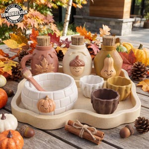 May include: A set of ceramic kitchenware featuring three lidded jars with autumn motifs, a large bowl with a pumpkin accent, and three small cups on a tray. The jars display a maple leaf, an acorn, and a pumpkin, all with smiling faces.