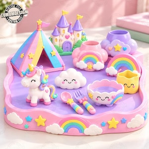 May include: A collection of pastel-colored decorative items including a circus tent, a castle, a unicorn figurine, a cloud-shaped bowl, a spoon, a fork, and rainbow-themed containers, all arranged on a pink tray with a rainbow and star motif.