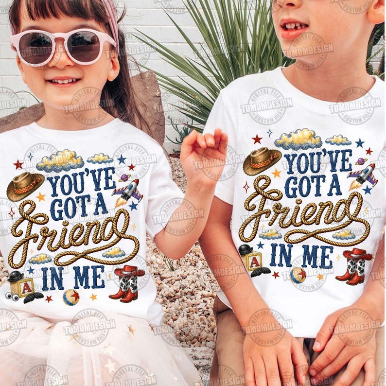 May include: Two white t-shirts featuring a graphic print with the text "YOU'VE GOT A FRIEND IN ME" in dark blue lettering. The design includes a brown cowboy hat, a coiled rope, a rocket ship, a toy block with the letter A, and cowboy boots.