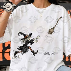 May include: A white t-shirt featuring a graphic of a witch in a black dress and hat running toward a flying broomstick. The witch has white hair and striped orange and black socks. The text "Well, shit..." is printed in black near the bottom right.