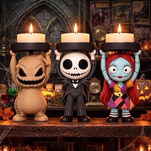 May include: Three decorative candle holders featuring stylised figures of Oogie Boogie, Jack Skellington, and Sally from The Nightmare Before Christmas. Each figure holds a black circular platform supporting a lit white tea light candle.