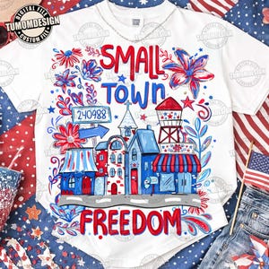 May include: White t-shirt with a colorful graphic design featuring a small town scene in red, white, and blue. The design includes the words "SMALL TOWN FREEDOM" and the number "240988".