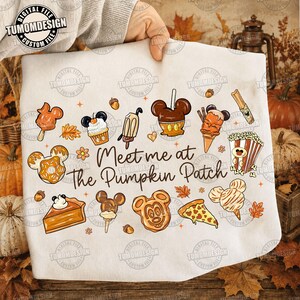 Op de afbeelding: Een wit t-shirt met de tekst Meet me at The Pumpkin Patch in bruin handschrift, omringd door diverse herfstachtige voedselillustraties zoals Mickey-vormige donuts, karamelappels, popcorn, taart en wafels met oranje accenten.