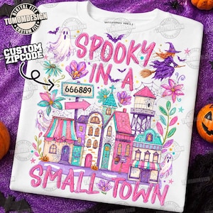 Puede incluir: Una camiseta blanca con un gráfico colorido de un pueblo pequeño con edificios rosas y azules, una torre de agua, fantasmas, una bruja en una escoba y flores. El texto dice SPOOKY IN A SMALL TOWN con una señal que muestra el número 666889.