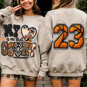 May include: Beige sweatshirt with a basketball design. The front has the text "My is on that COURT" with a heart-shaped photo and basketball graphics. The back shows the number "23" in an orange basketball design.