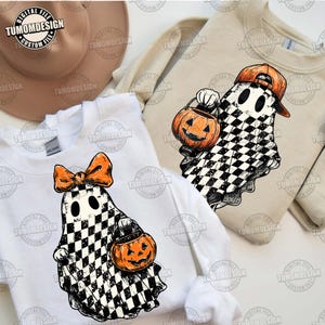 May include: Three sweatshirts with Halloween-themed designs. One white sweatshirt features a ghost with a checkered pattern, an orange bow, and a pumpkin bucket. Another sweatshirt is beige with a ghost wearing a cap and holding a pumpkin. The text "TUMOMDESIGN" is visible.