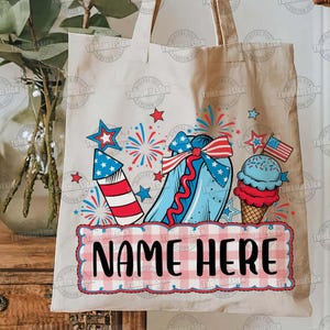 May include: A beige tote bag featuring a patriotic design with a red, white, and blue color scheme. The design includes a firework, a hot dog, an ice cream cone, stars, and the text "NAME HERE" in a checkered frame. The bag has two handles.